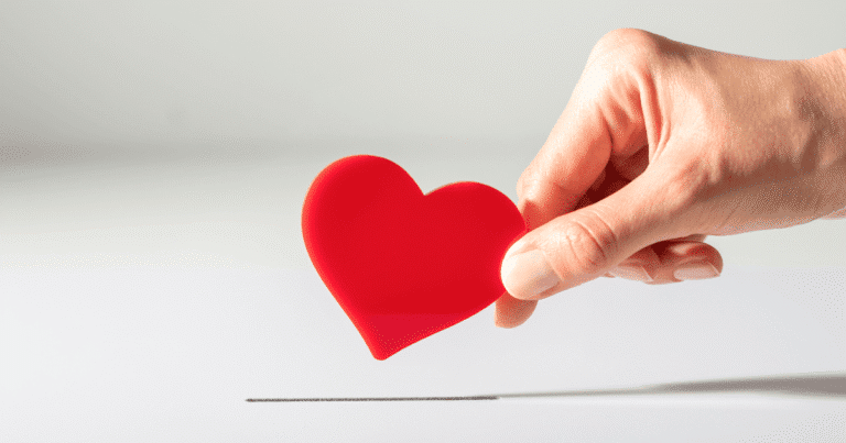 Mano metiendo un corazón rojo en una hucha de donación