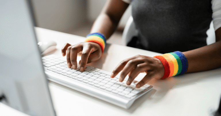 Manos escribiendo en teclado con una muñequera de colores LGTBI+