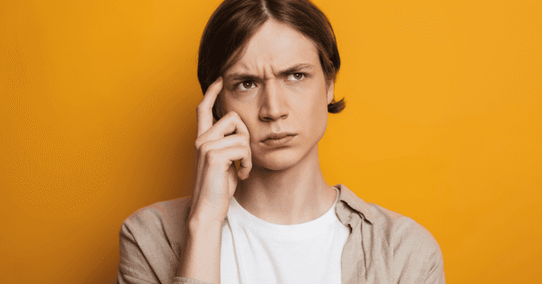 Primer plano de un joven con actitud pensativa, con la mano apoyada en la cabeza y gesto de duda frente a una pantalla de ordenador. La imagen representa el proceso de decisión de una asociación u ONG al elegir entre un blog o una web para su estrategia digital.