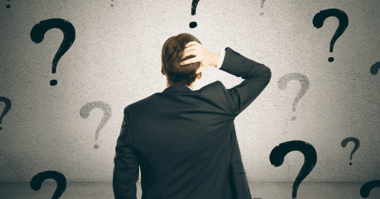 Hombre de espaldas con gesto de duda frente a una pared llena de interrogantes, representando la indecisión al elegir entre un dominio .com o .es.